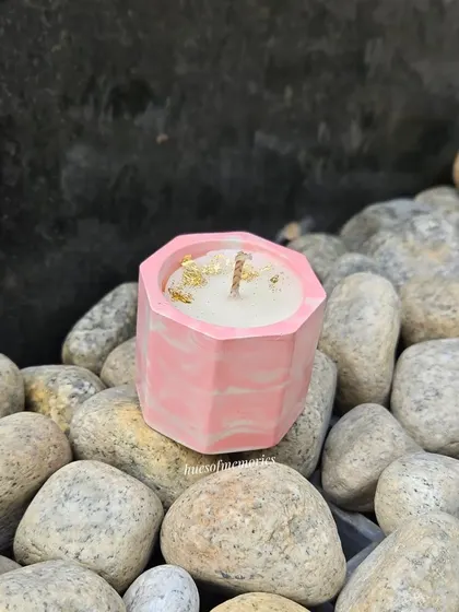 A single hexagon candle in a pink marble pattern, placed among natural stones. The wooden wick and gold foil flakes add a rustic yet elegant touch.