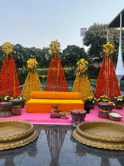 This poolside Haldi decor at Udman Greater Noida features vibrant marigold cones in orange and yellow. The setup is completed with traditional brass urlis and colourful seating, reflecting beautifully on the water.