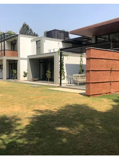 A farmhouse project in progress, showing the relationship between the built structure and the expansive lawn. The design uses clean lines and natural materials like rammed earth walls to complement the rural setting.