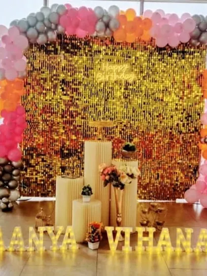 A bright and cheerful setup with a gold sequin wall and a pink, orange, and silver balloon garland.