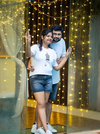 A happy and casual portrait of a couple framed by a doorway and a curtain of fairy lights.