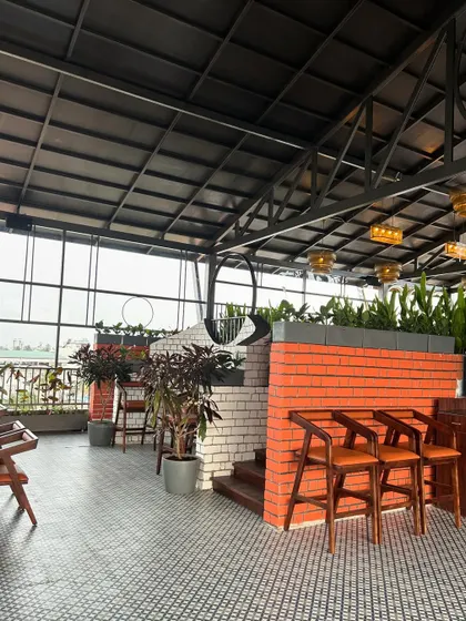 This view of 'The Soda Factory' highlights the use of potted plants with dark foliage to complement the red brick and white-painted walls. The planters add visual interest and help to define the bar and seating areas.
