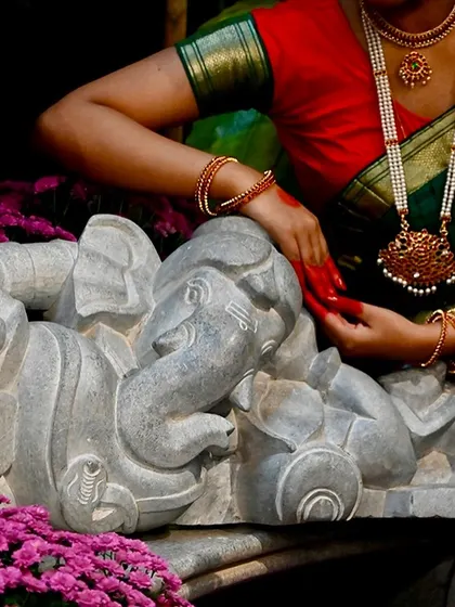 A moment of connection between art and tradition, as a dancer's hands grace our reclining Ganesha statue during a festival.