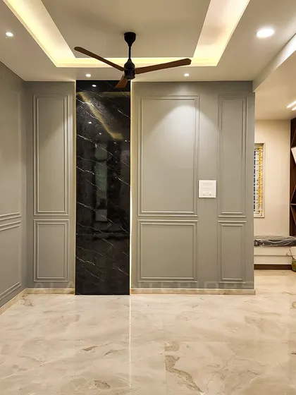 A minimalist foyer featuring elegant grey wall molding and a striking black marble accent panel. In the background, a custom-designed unit with geometric patterns adds a touch of artistic flair to the entrance.