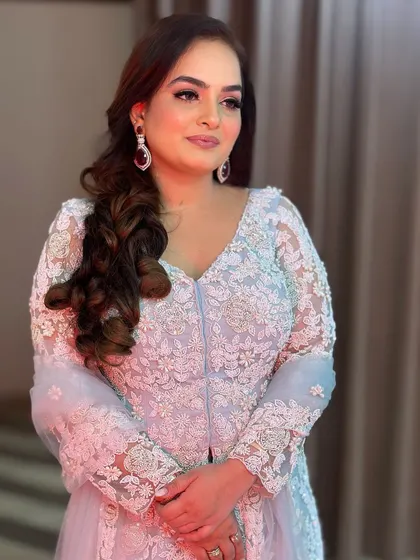 A client looking elegant and poised in a beautiful light blue embroidered outfit, with her hair styled to the side in soft curls.