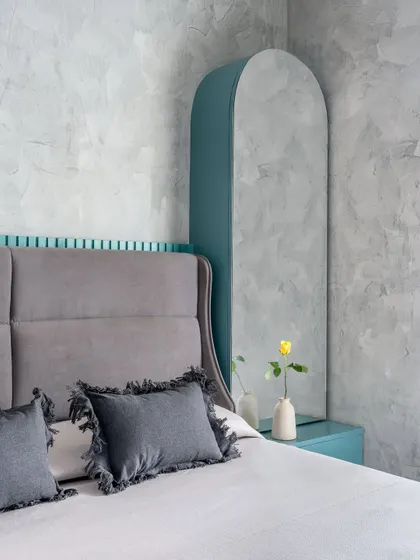 A detail shot of the arched dressing mirror and teal bedside unit in the matriarch's room. The combination of textures, from the concrete wall to the fluted paneling, is key to this design.