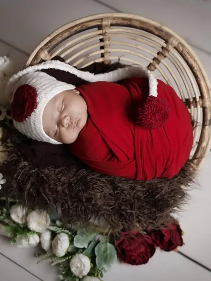 A cozy winter-themed newborn photo. The baby is wearing a cute pom-pom hat while nestled in a basket, creating a warm and festive feel.