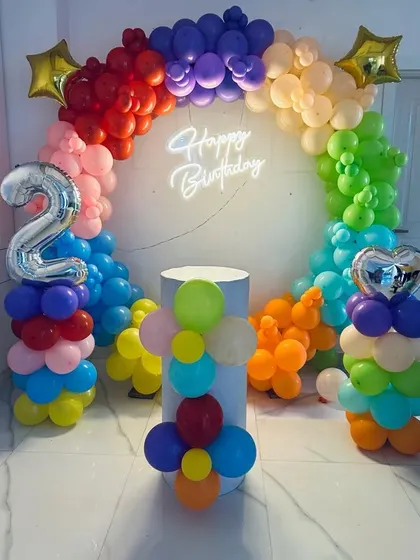 A rainbow-colored balloon arch for a 2nd birthday, complete with a neon sign and balloon columns.