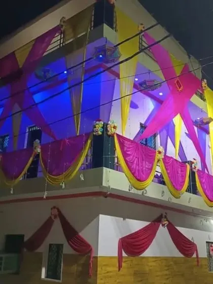 A house facade decorated at night with pink and yellow drapes in a criss-cross pattern, illuminated by blue and purple lights.