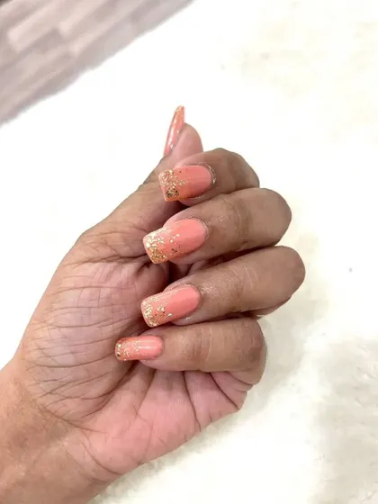 A hand-held shot of the peach and glitter nails, highlighting the square shape and the delicate sparkle.