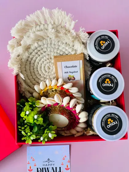 This red box hamper is filled with healthy Omay snacks, a chocolate bar, macrame coasters, and shell-work t-light holders.