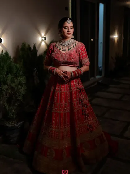 A full-length portrait of the bride in her stunning red lehenga, captured at night with beautiful architectural lighting.