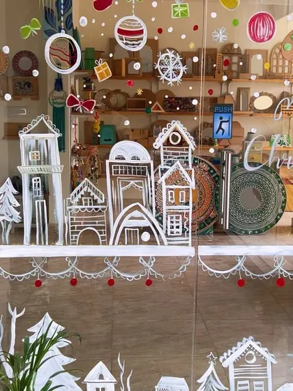 A close-up of my studio's Christmas glass mural, with hand-painted winter houses and festive ornaments.