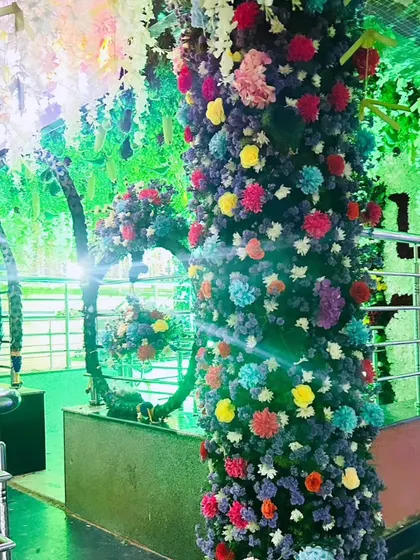 A pillar wrapped in colorful flowers, part of a larger temple decoration scheme, illuminated with bright green light.