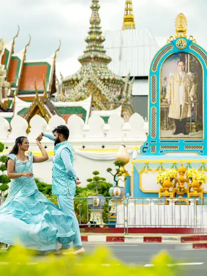 A playful, dynamic shot in front of the Grand Palace in Bangkok, with the couple in matching blue outfits that pop against the scenery.