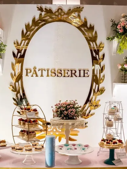 A beautiful Parisian 'Pâtisserie' dessert table. The elegant gold-framed signage, tiered cake stands, and delicate floral arrangements make for a delicious and stylish display.