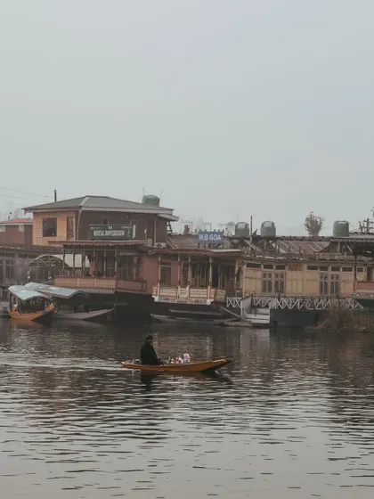 A wide shot of the houseboats on Dal Lake, with a lone shikara passing by. The scene captures the unique lifestyle of this region.