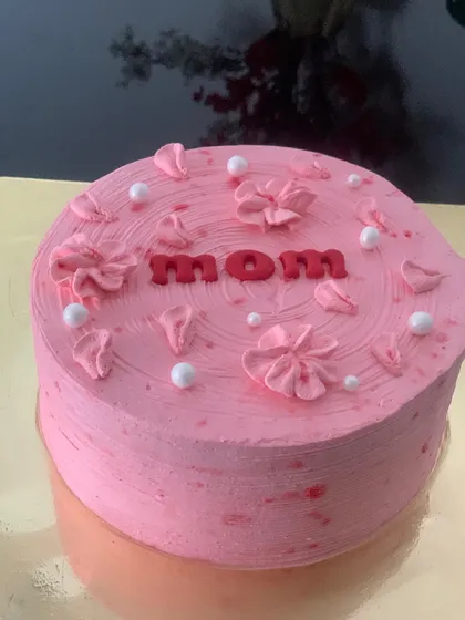 A simple and sweet pink cake for Mom. The cake is decorated with the word "Mom" and delicate pink flower petals.