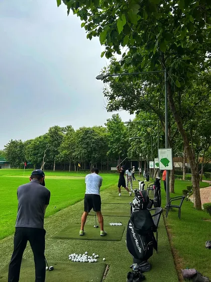 A view from behind the tee line, showing a group of golfers practicing together on a cloudy day.