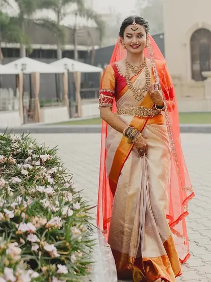 My bride Brunda looks like a queen in this off-white and orange Kanjivaram saree, paired with a custom red blouse and a sheer red veil.