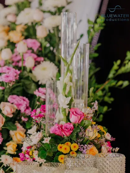 A close-up of a floral centerpiece with pink and yellow roses and tall glass candle holders.
