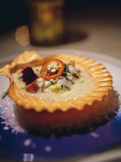 A beautifully plated seafood appetizer in a crispy shell, garnished with a chili slice.