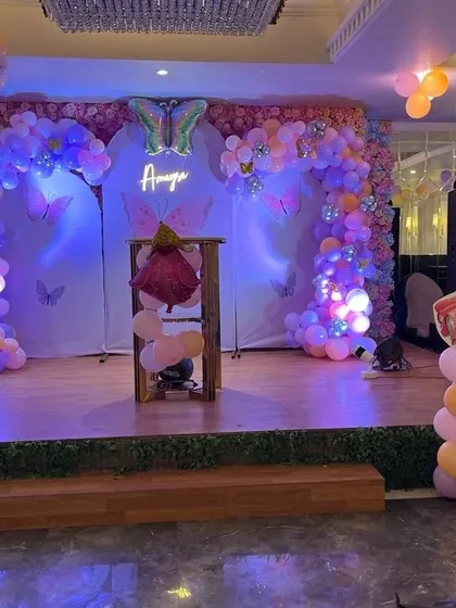 A butterfly and princess themed stage decoration. This setup features two balloon arches, a personalized neon sign, and a princess cutout.
