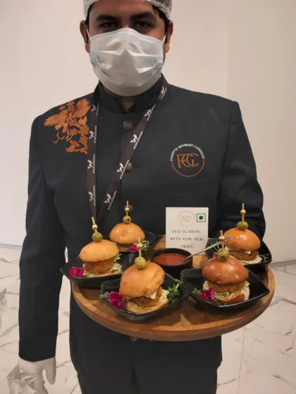 Our staff presenting mini Veg Sliders with Peri Peri Mayo. These small bites are perfect for mingling, offering a familiar comfort food with a spicy, gourmet twist, served on a platter with individual portions.