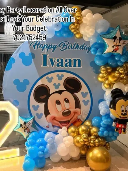 A classic that never goes out of style: a Mickey Mouse birthday party. This decoration features a custom circular backdrop with Mickey, a blue and gold balloon garland, and a light-up number '2' for Ivaan's birthday.
