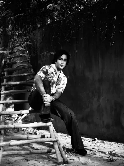A classic black and white portrait of Zahan Kapoor seated on a bamboo ladder, creating an interesting and rustic composition.