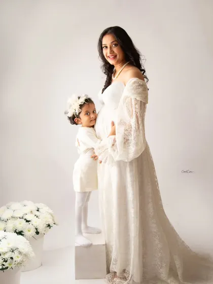 An angelic family portrait in all white. The older sister stands on a block to give her mom's baby bump a sweet hug.