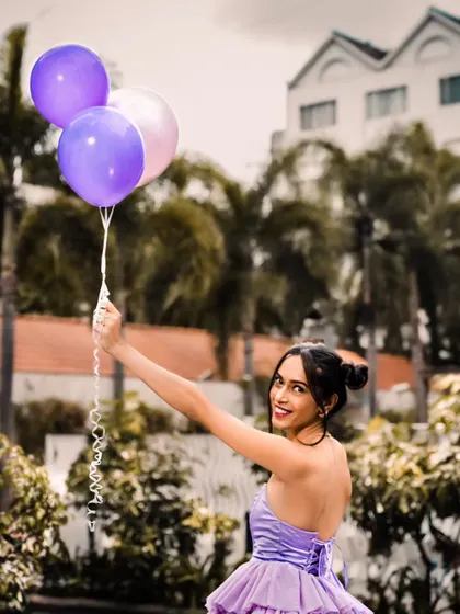 Holding the balloons high and smiling back at the camera.