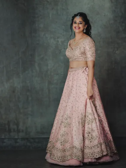 A full-length studio shot of a pastel pink embroidered lehenga. The classic pose and clean background provide a clear and elegant view of the entire ensemble for a portfolio.