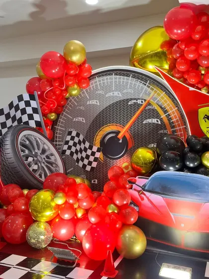 A close-up of the Ferrari decor, highlighting the tire prop, checkered flag, and red and gold balloon clusters.