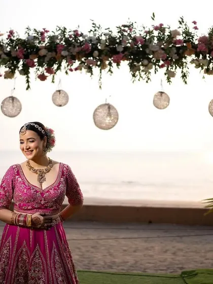 A joyful portrait of the bride at her beachside wedding venue, standing before the beautiful floral arch.