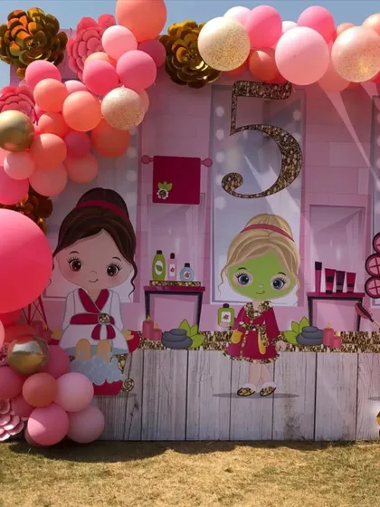 A fun and girly spa-themed 5th birthday party. The backdrop features cute cartoon characters at a spa, framed by a pink and orange balloon garland for a day of pampering and fun.