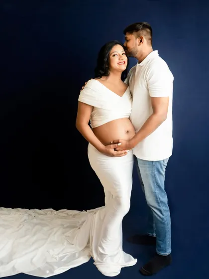 A classic couple's pose against a solid deep blue backdrop. The simplicity of the setting puts all the focus on the parents-to-be.