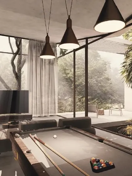 The family room in the House of Veils is a cozy, intimate space for relaxation. It features a pool table and comfortable seating, all while being connected to the outdoors through an internal courtyard and large windows.