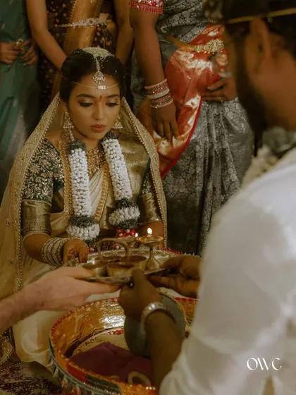 A candid, over-the-shoulder view of a bride during a traditional South Indian wedding pooja, her expression full of devotion.