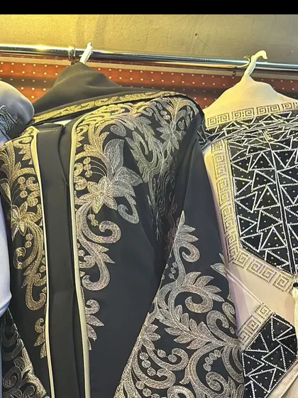 For those who love a bold statement, this black abaya with heavy gold embroidery is a showstopper. Next to it is another piece with a geometric black and white pattern.