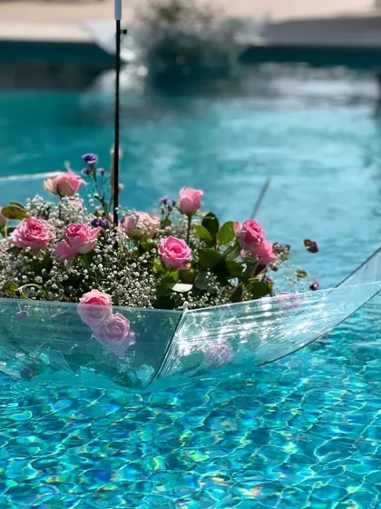 A creative and whimsical decor idea: a clear umbrella filled with pink roses and baby's breath, floating gracefully in a swimming pool.