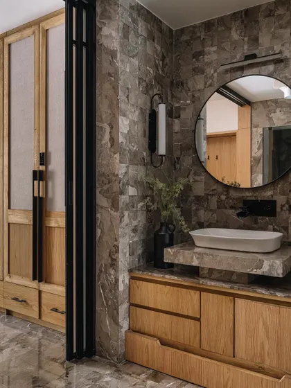 This bathroom in Cocoon House is a rich tapestry of textures. We combined heavily veined grey marble walls with a light wood vanity and a fabric-paneled wardrobe, creating a luxurious and tactile space that feels both modern and timeless.