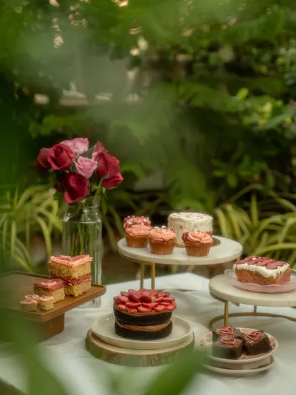 A beautiful outdoor setup for a Valentine's Day collection of cakes and cupcakes. The natural greenery and soft lighting create a romantic and whimsical atmosphere for this bakery photoshoot.