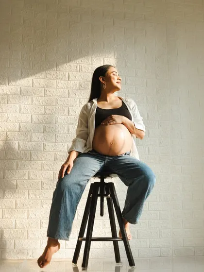 A relaxed and confident lifestyle shot. The casual outfit of jeans and a top, combined with the warm studio light, creates a modern and authentic portrait.