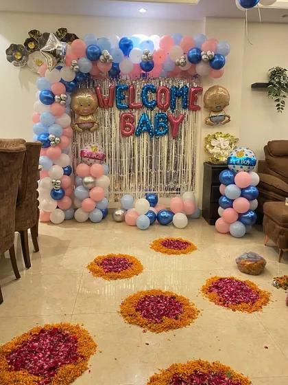 A 'Welcome Baby' home decoration. I create a festive atmosphere with a balloon backdrop, 'Welcome Baby' foil letters, and traditional marigold and rose petal rangoli on the floor.
