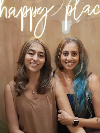 Two friends showing off their new hairstyles. One has a chic, natural look, while the other sports a fun pop of blue.