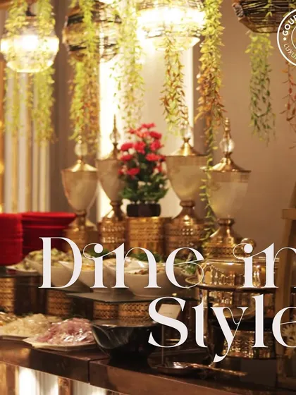 "Dine in Style." A beautifully arranged buffet with hanging greenery and elegant gold serving dishes. We turn every meal into a stylish affair.
