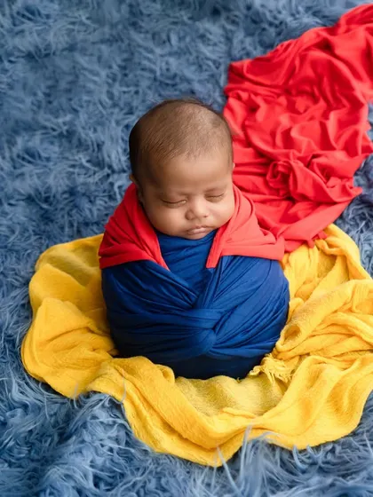 A fun take on a superhero theme, with a newborn swaddled in blue and red wraps to resemble Superman's costume.