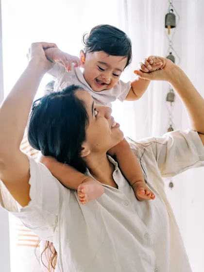 A mother lifting her laughing baby, with light streaming in from the window. A joyful and light-filled image.
