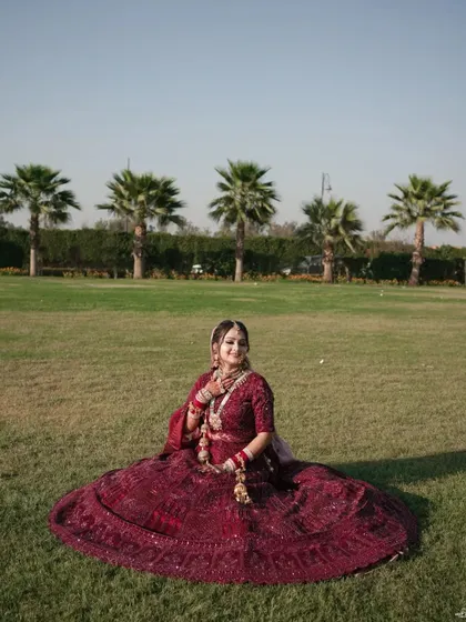 A beautiful bridal portrait taken outdoors, with her magnificent lehenga spread out on the grass, set against a backdrop of palm trees.